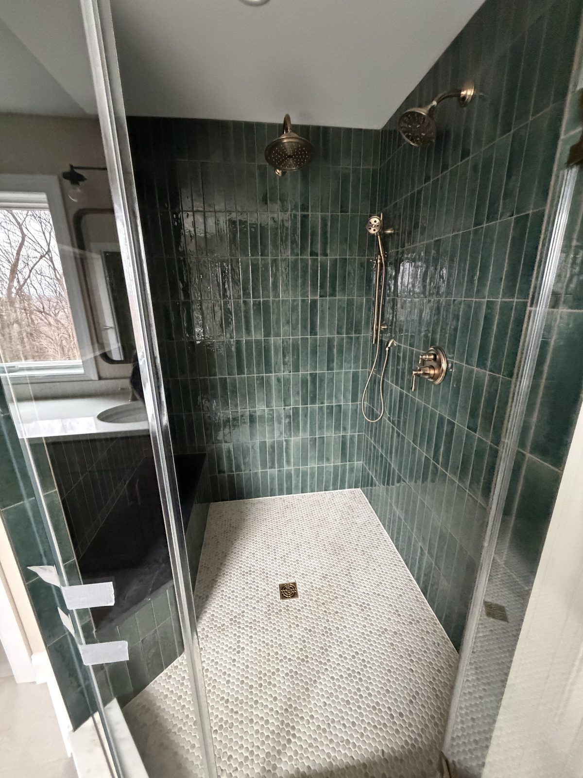 Green tile shower stall with dual rain heads and penny tile floor